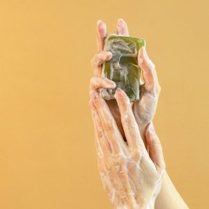 Close-up of hands washing with bar soap against a yellow background for hygiene and cleanliness.