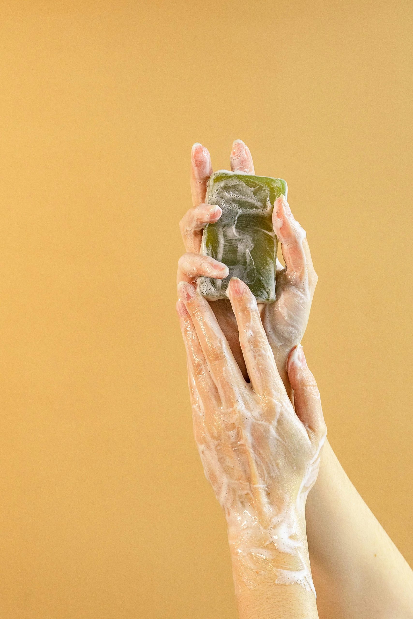 pexels photo 7814648 7814648 Close-up of hands washing with bar soap against a yellow background for hygiene and cleanliness.